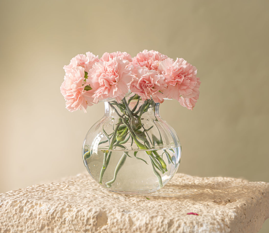 Clear round vase full of pink delphiniums standing on a pedestal  