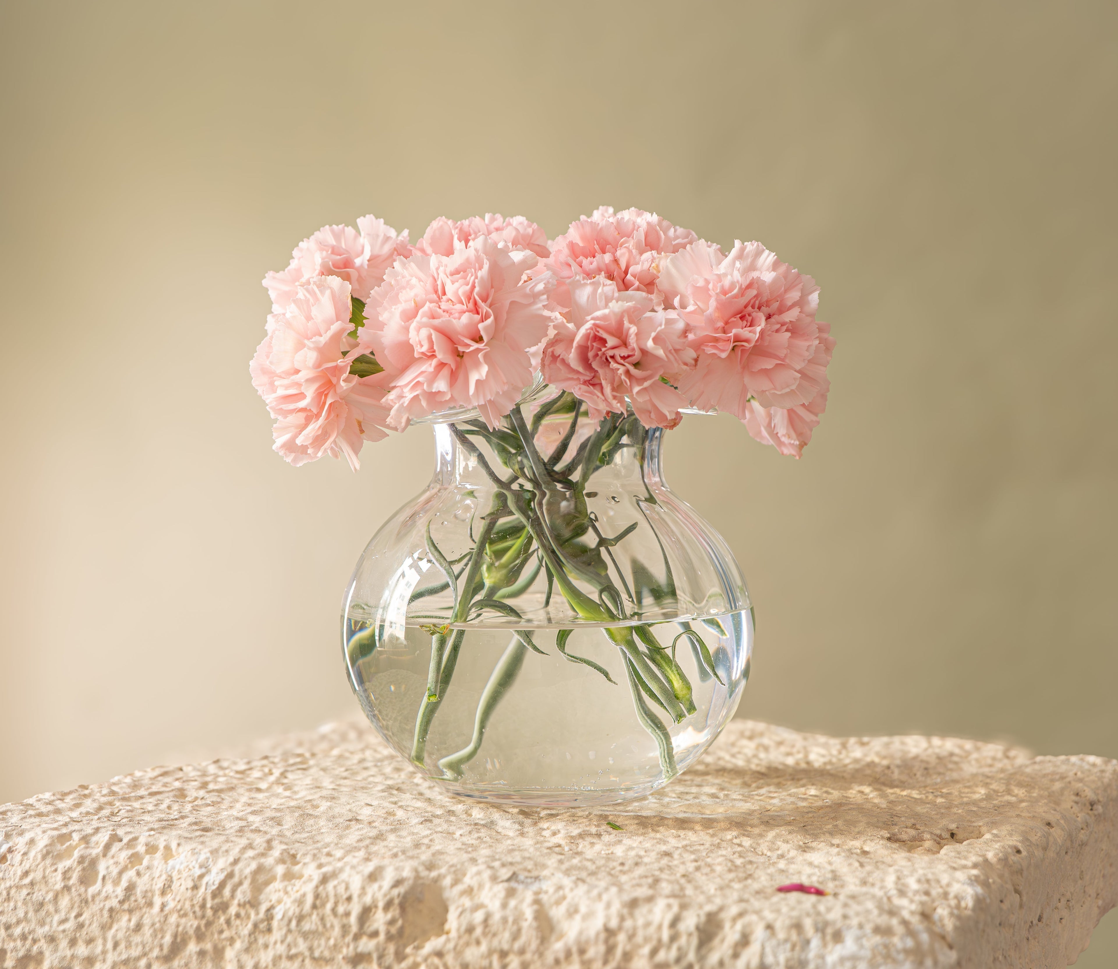 Clear round vase full of pink delphiniums standing on a pedestal  