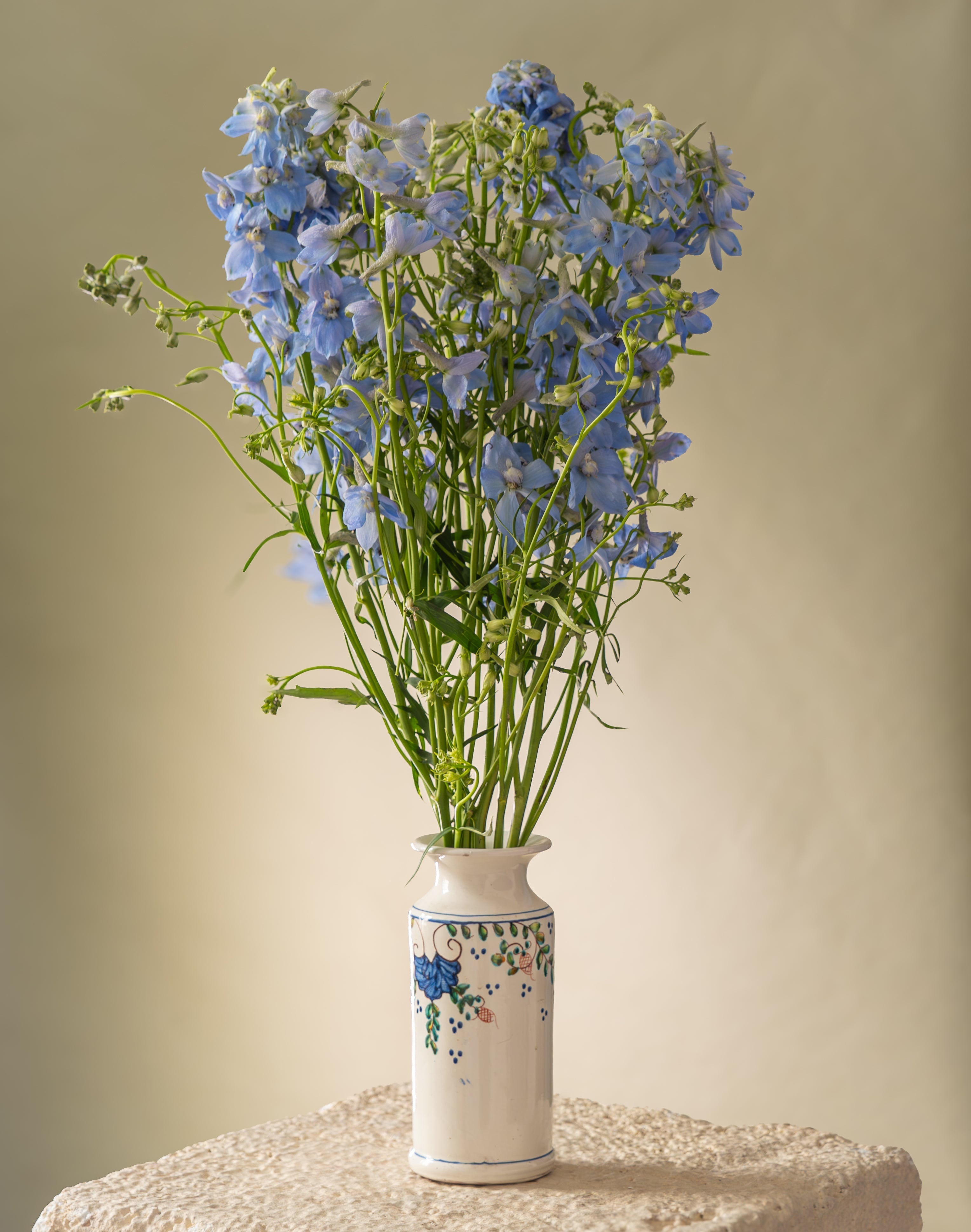 White vase full of blue delphiniums standing on a pedestal  