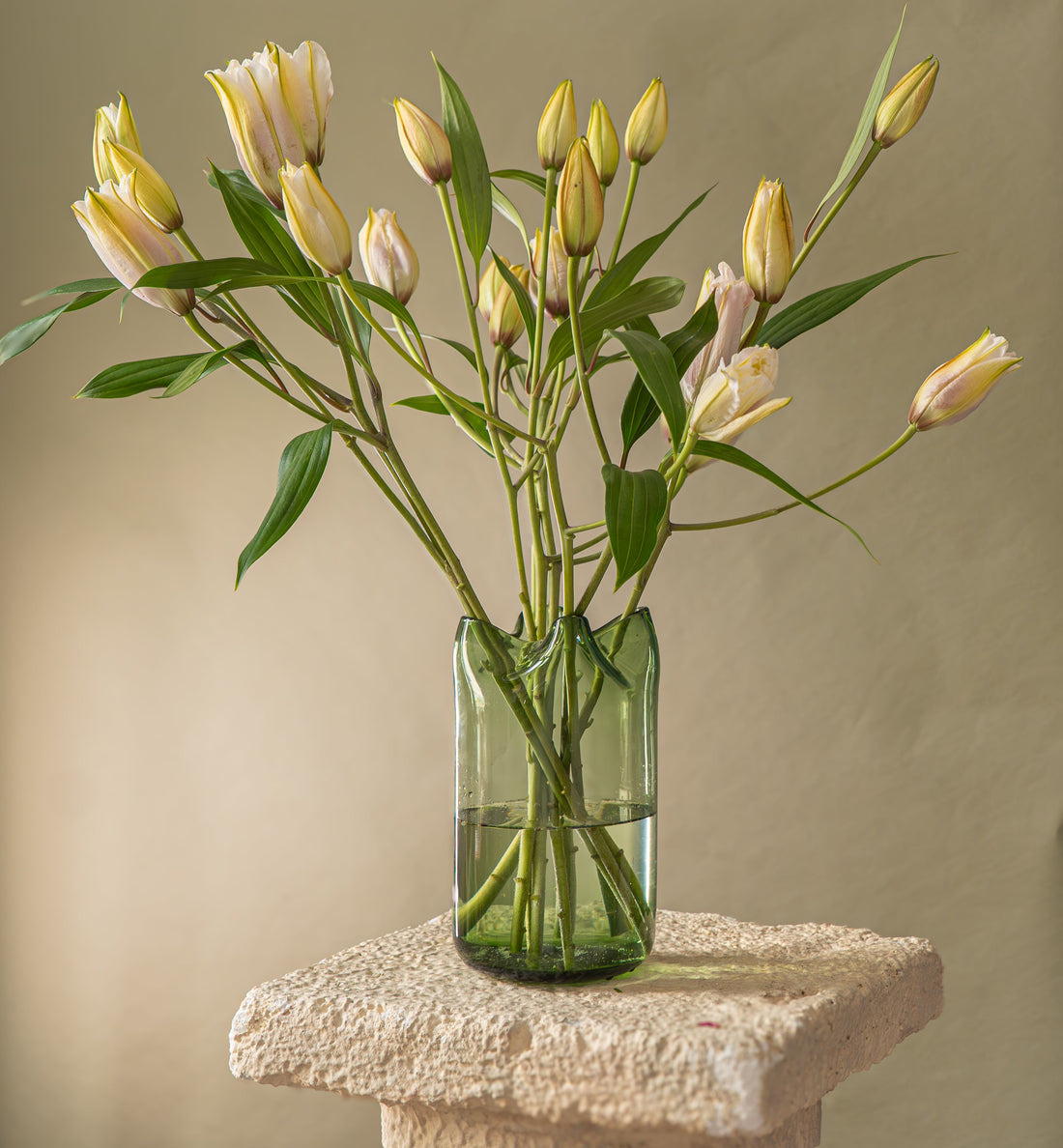 Green clear vase full of lilies standing on a pedestal 