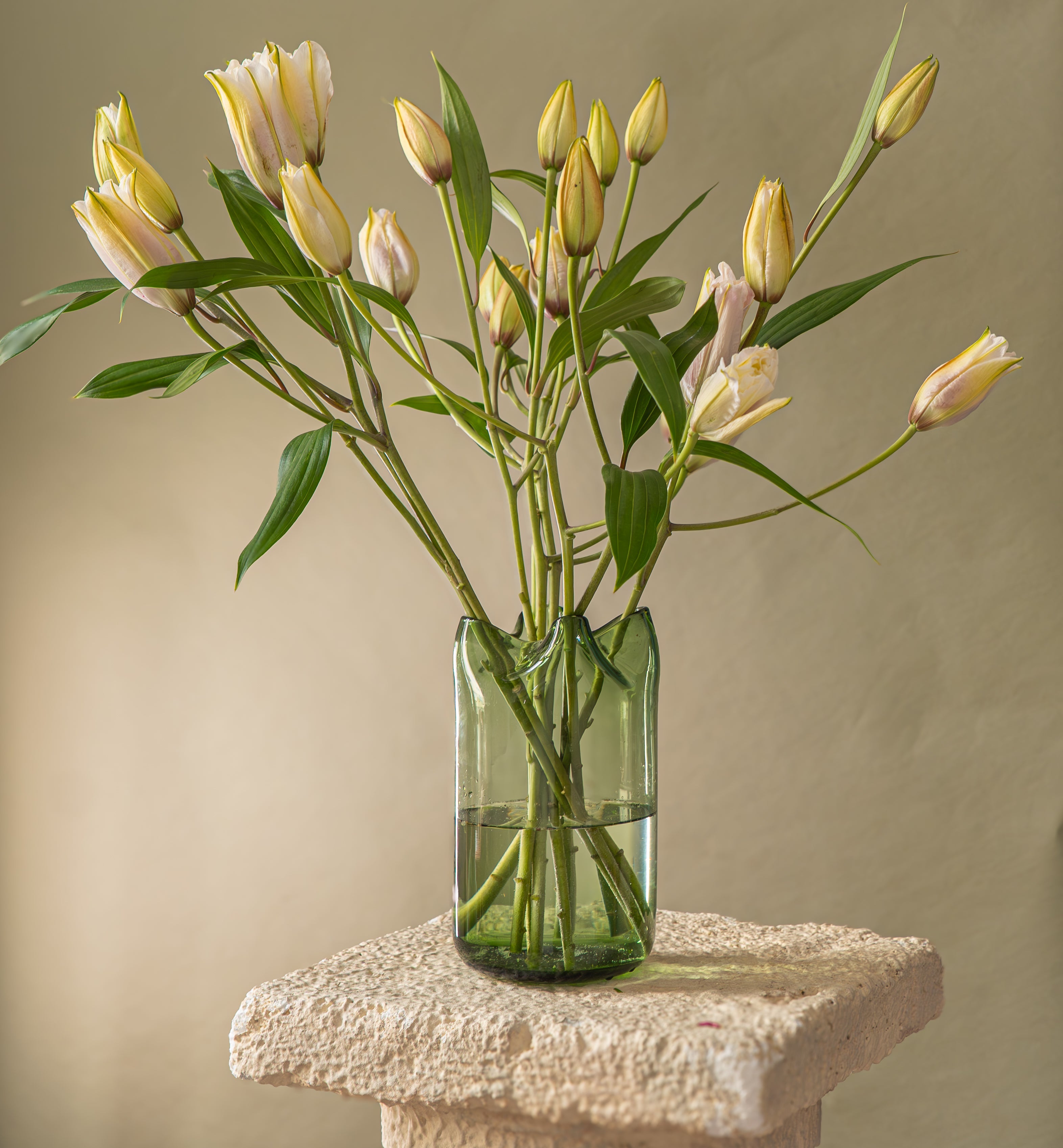 Green clear vase full of lilies standing on a pedestal 