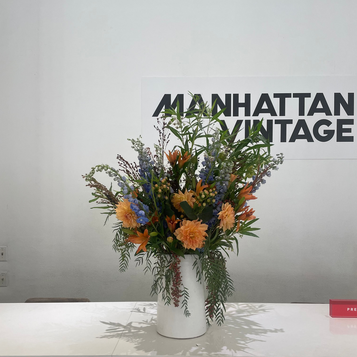 Floral arrangement in a white vase on a gray surface with 'Manhattan Vintage' branding in the background.