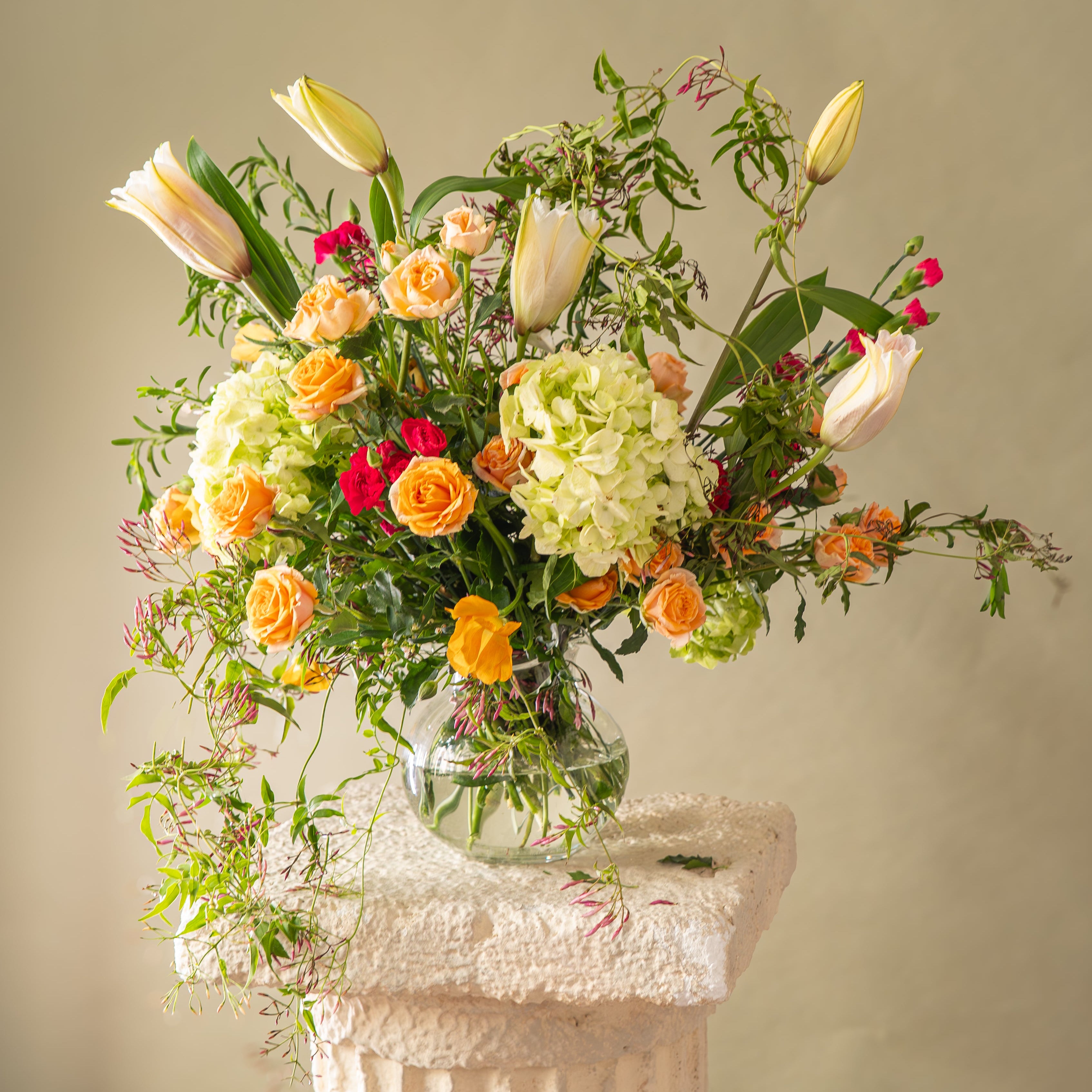 Bouquet of flowers in a clear vase on a decorative pedestal against a neutral background